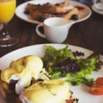 Eggs Benedict with greens, fresh orange juice and pancakes on a cozy brunch table