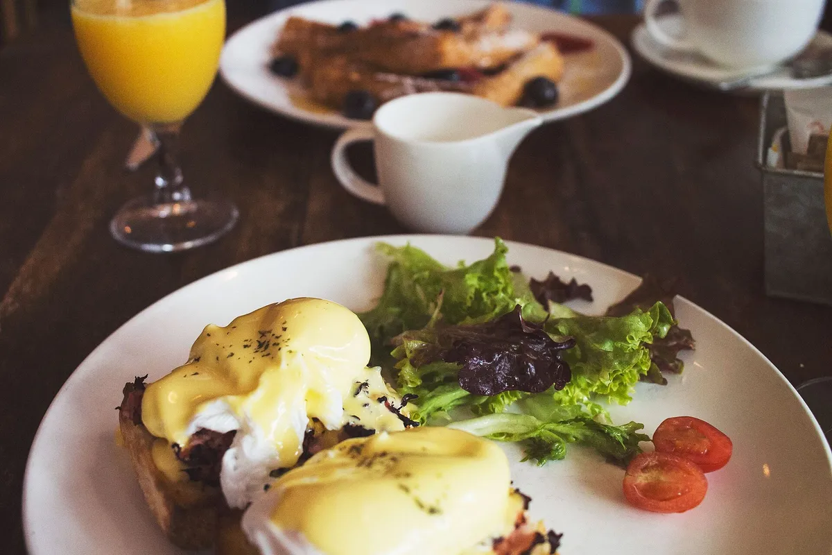 Eggs Benedict with greens, fresh orange juice and pancakes on a cozy brunch table