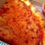 Classic New York style cheese pizza slices in a takeout box with sauce