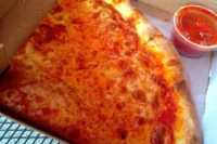Classic New York style cheese pizza slices in a takeout box with sauce